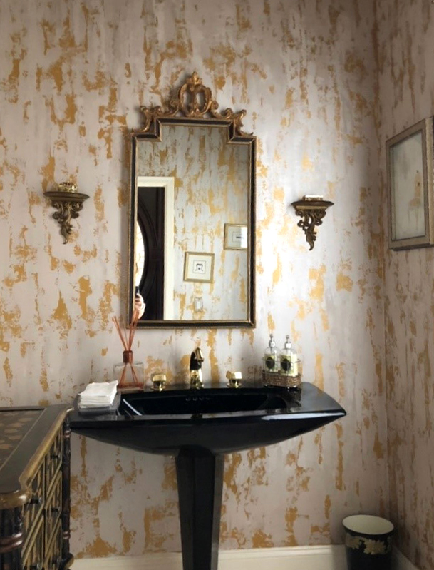This powder room is based in gold and has a plaster pulled vertically to give it its interest and height in the room. The black helps make the finish pop!