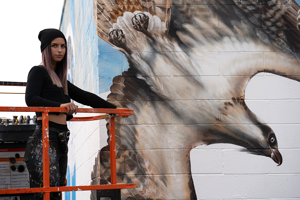 Muralist Tori Immerwahr next to the painted osprey on the corner of her Impact mural.